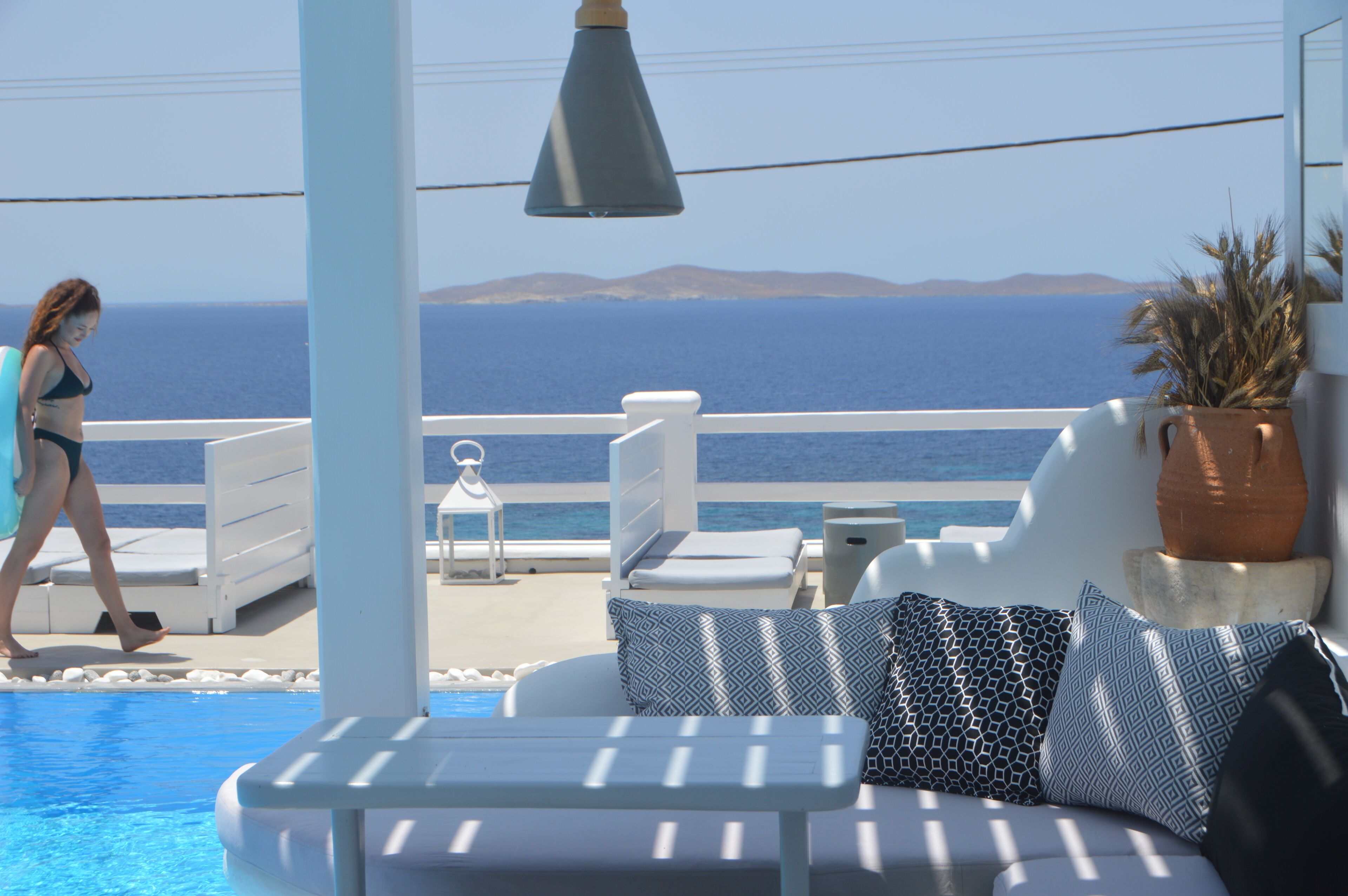 A poolside area with a sofa, a potted plant, and a view of the sea.