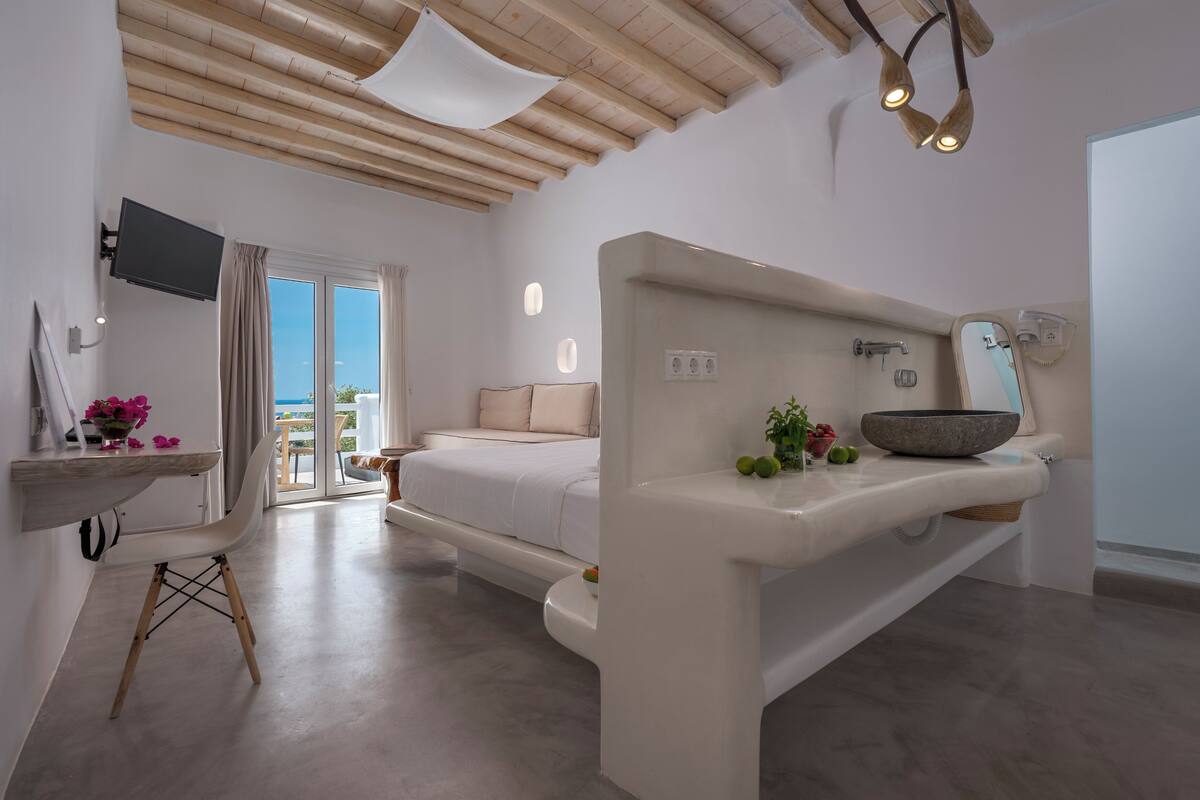 A modern bedroom with a large bed, a bedside table with a bowl, a mirror, and a TV mounted on the wall.