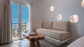 Ein modernes Zimmer mit einer Couch, einem hölzernen Hocker und Meerblick durch große Glasfenster.