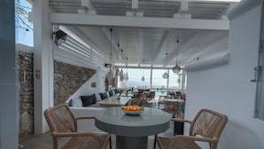 A modern outdoor seating area with wicker chairs, a round table with fruit, and a stone wall. - Flaskos Luxury Suites (Mykonos)