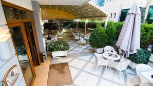 A hotel patio with outdoor seating, potted plants, and a covered area. - Kotoni (Tirana)