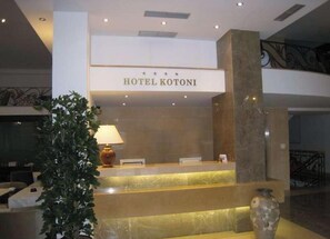 Una recepción con un letrero que dice 'HOTEL KOTONI' y un florero a la derecha.