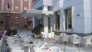 A hotel patio with outdoor seating, a covered area, and a building with large windows. - Kotoni (Tirana)