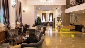 A lobby with a reception desk, seating area, chandeliers, and a staircase. - Kotoni (Tirana)