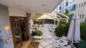 A hotel patio with outdoor seating, a glass entrance, and a view of the cityscape. - Kotoni (Tirana)