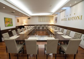 Un salón de conferencias con una larga mesa, varias sillas y un cartel que dice 'HOTEL KOTONI' en la pared.