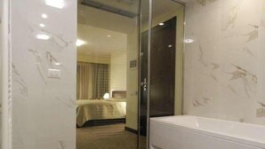 A hotel room with a glass door leading to a bedroom, a white bathtub, and a marble-patterned wall. - Kotoni (Tirana)