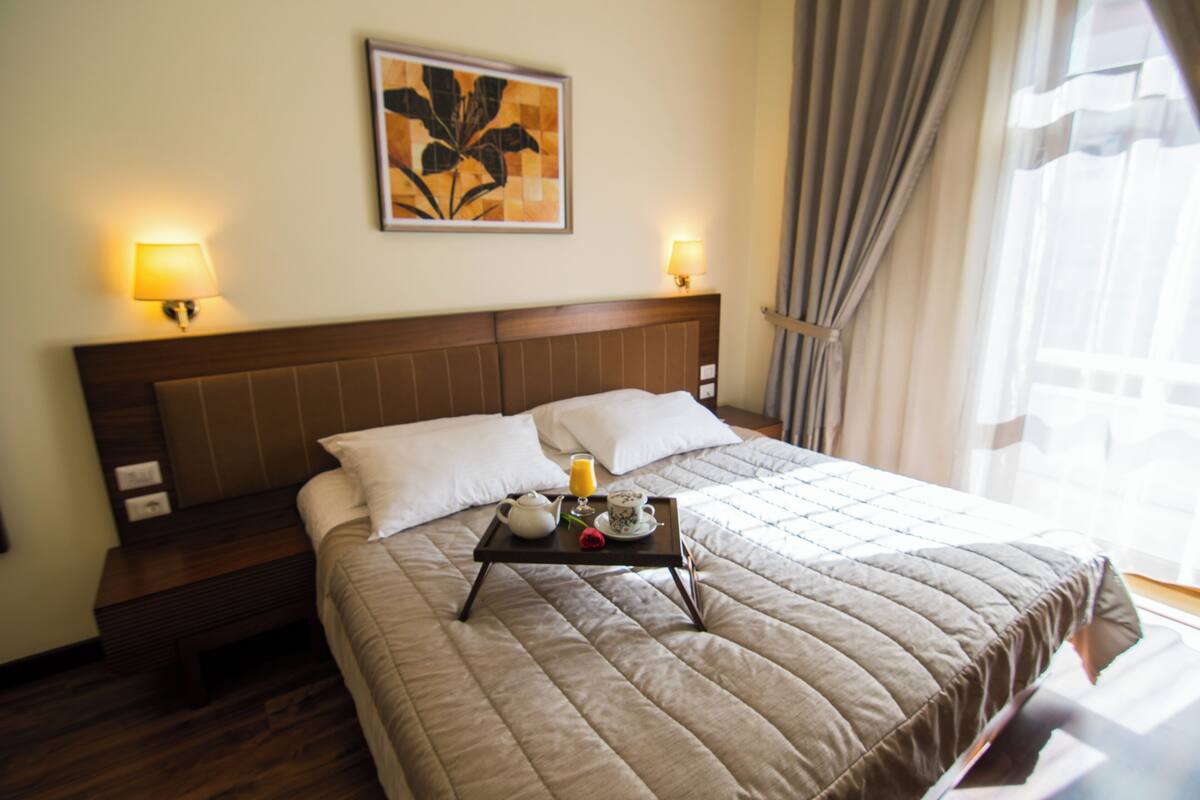 Une chambre d’hôtel avec un grand lit, des lampes de chevet, un plateau avec des articles pour le petit-déjeuner et un tableau floral accroché au mur.