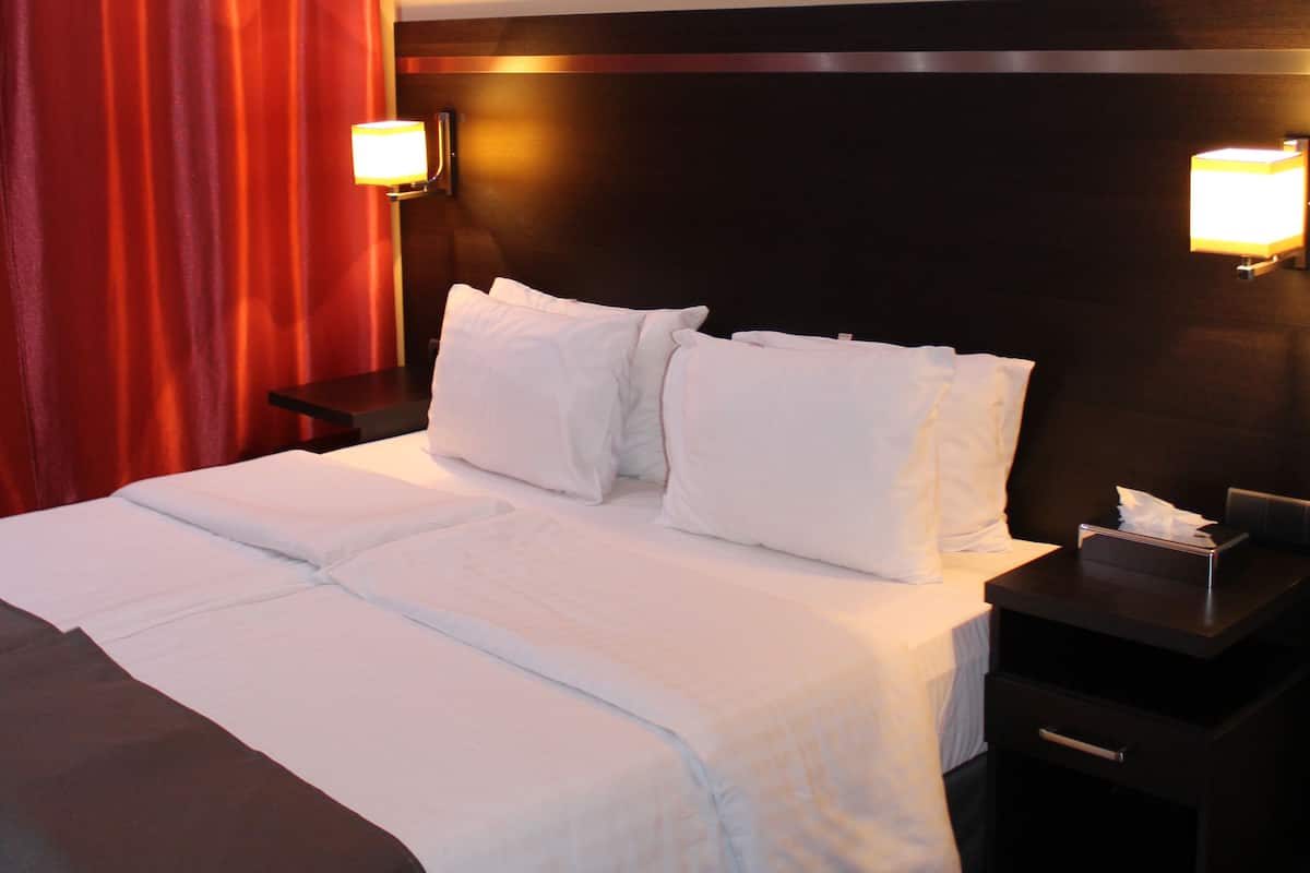 Habitación de hotel con una cama grande, dos mesitas de noche, una lámpara de noche y cortinas rojas, además de lámparas fijadas a la pared.