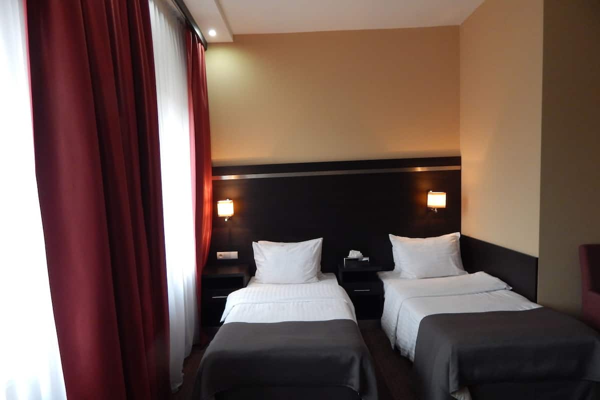 Una habitación de hotel con dos camas, un cabecero oscuro, lámparas de noche y una cortina roja.