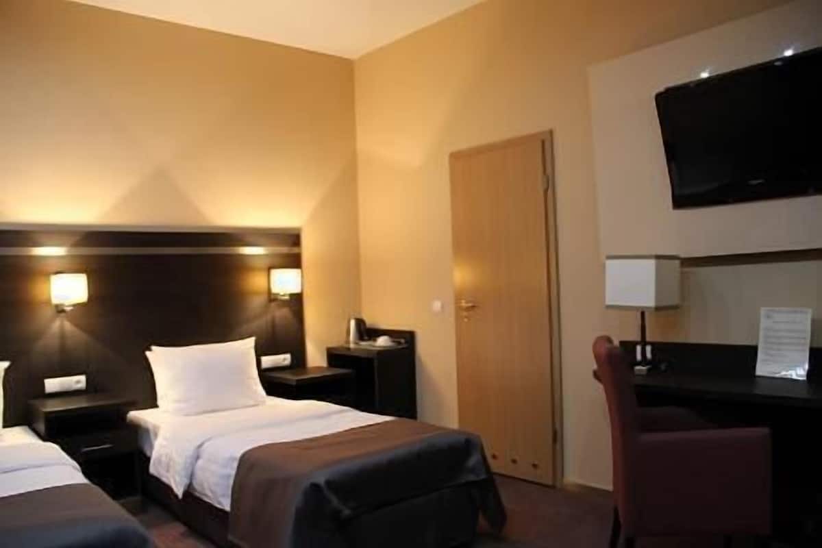 Habitación de hotel con dos camas, un escritorio, una silla, un televisor y una puerta.
