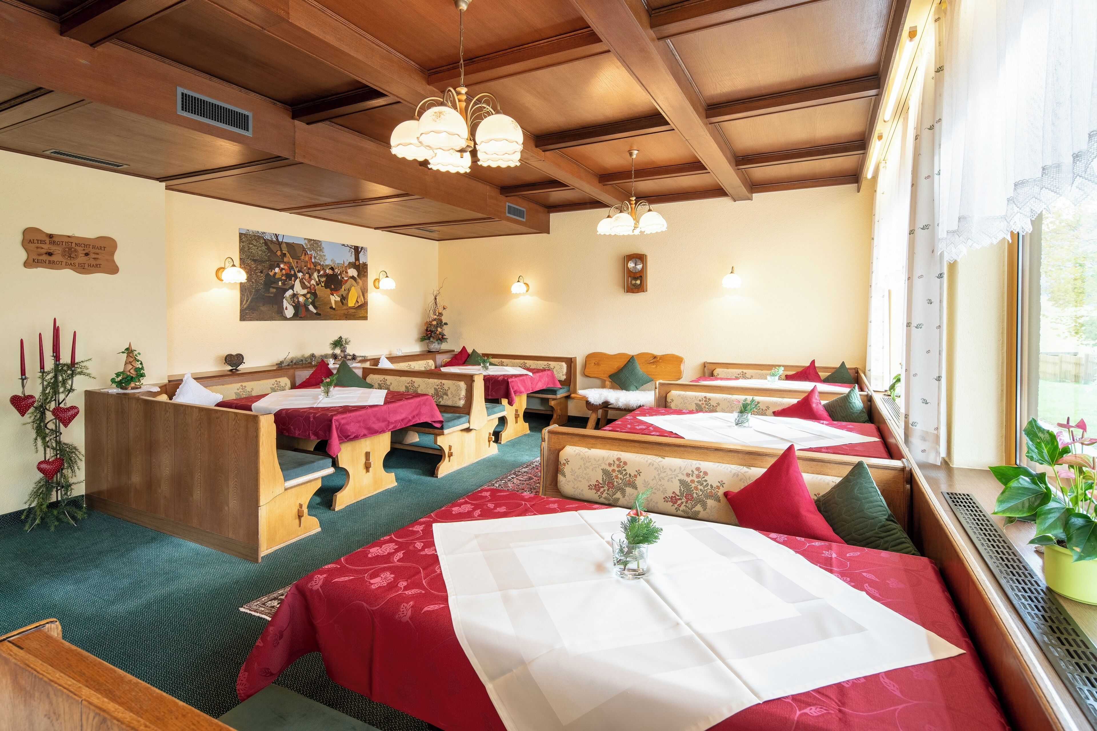 A cozy restaurant with wooden benches and tables, decorated with red and white linens, and a large painting on the wall.