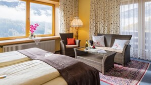 Habitación de hotel con cama, dos sillones, un sofá, una mesa y vistas a montañas a través de una ventana.