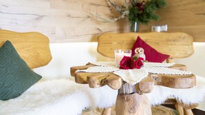 Una cama de madera con una colcha blanca y esponjosa, un taburete de madera pequeño con un paño blanco y una rosa roja, y un jarrón con flores al fondo.