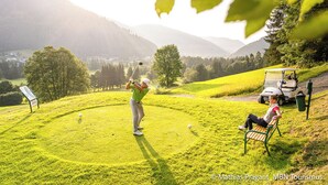 Un campo de golf con una persona jugando, un carrito de golf y un banco.