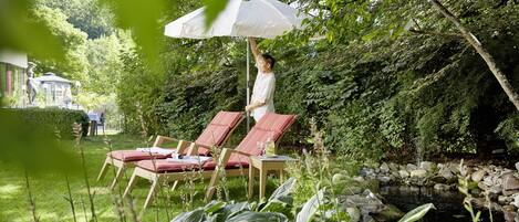 Un jardin avec un bassin, des fauteuils de jardin rouges et un parasol blanc.
