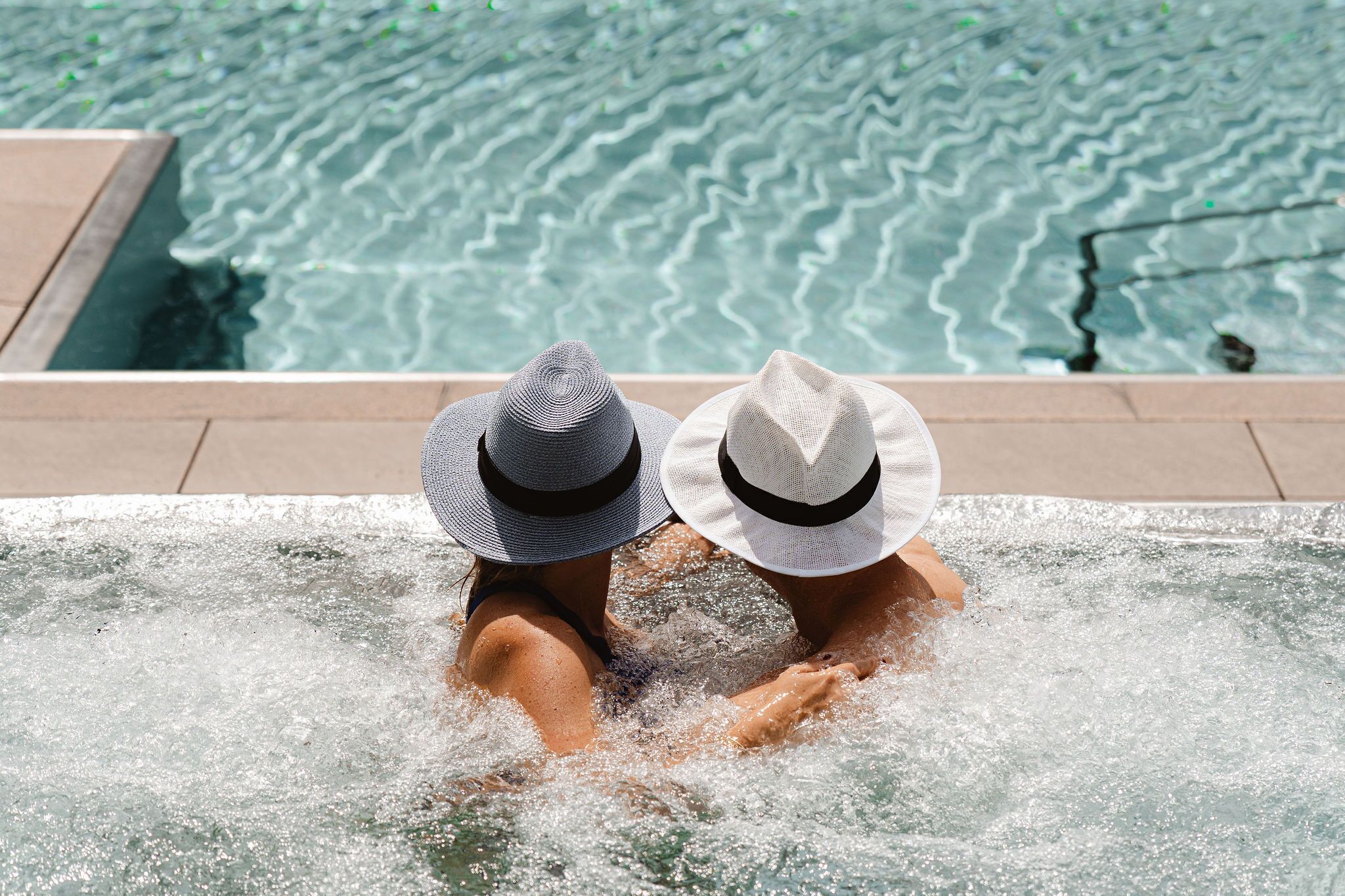 Two people in a hot tub with a view of a pool.
