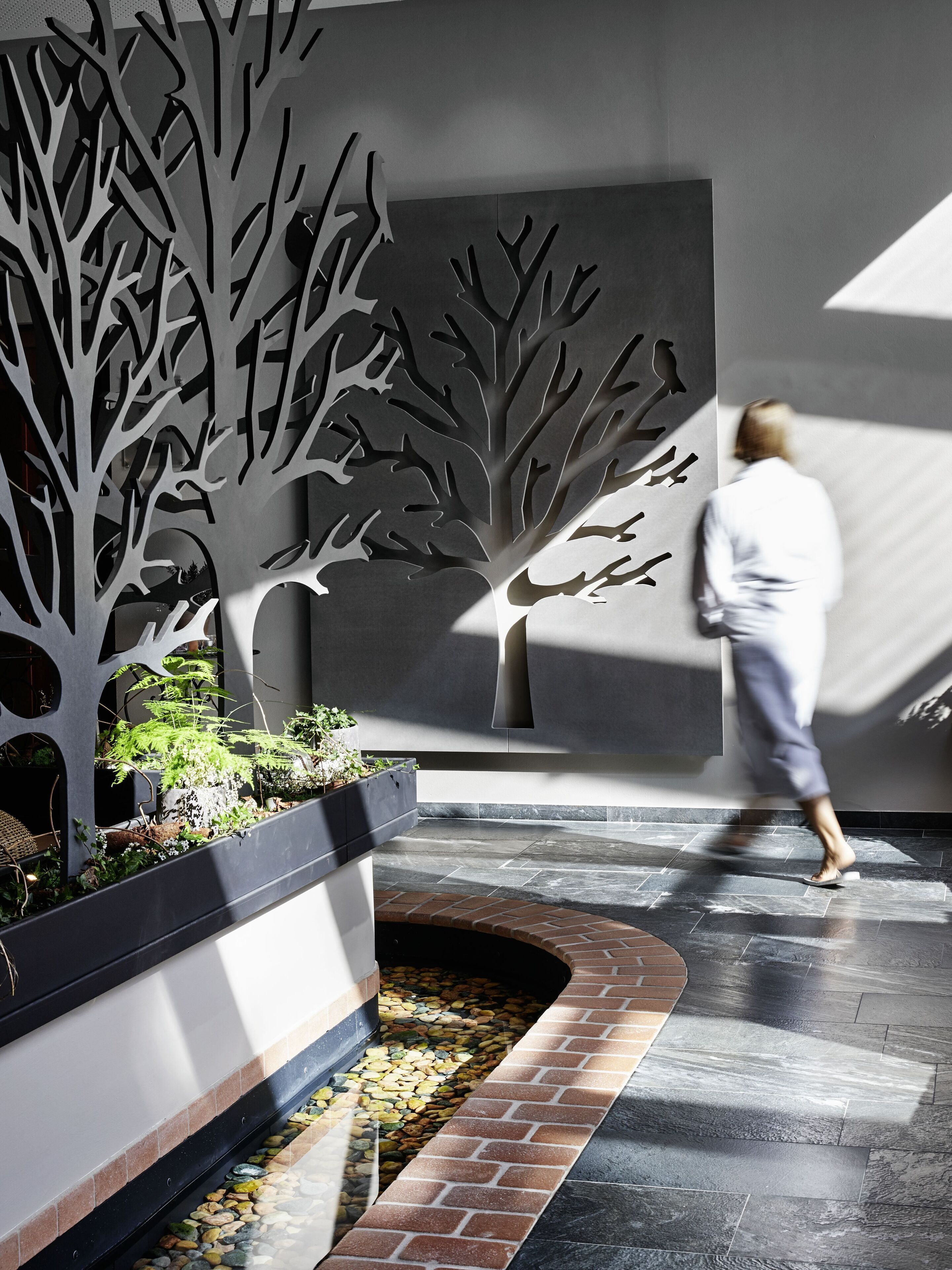 A modern indoor space with a central tree-like structure, a brick pathway, and a person walking.