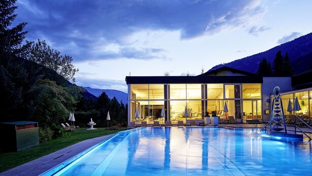 A modern hotel with a swimming pool, outdoor seating, and a mountain backdrop.