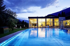 A modern hotel with a swimming pool, outdoor seating, and a mountain backdrop. - DAS RONACHER Thermal Spa Hotel  (Bad Kleinkirchheim)