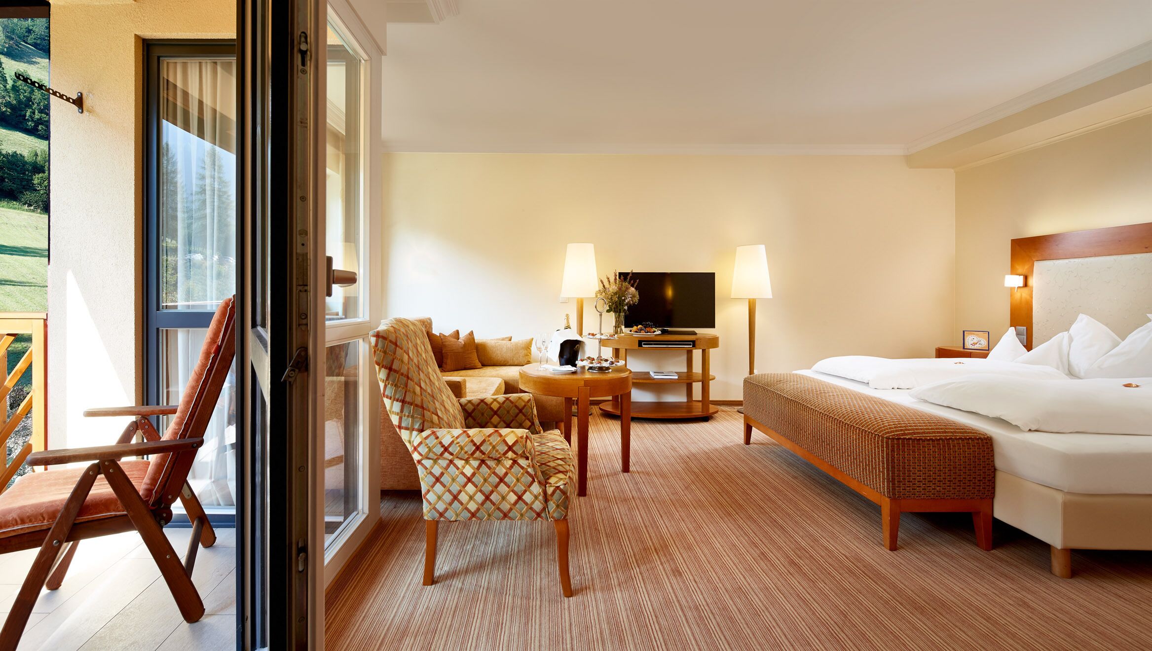 Une chambre d’hôtel comprenant un lit, un canapé, une chaise, une petite table, une télévision et un balcon.