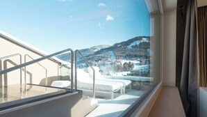 A balcony with a glass wall, a hot tub, and a view of snow-covered mountains.