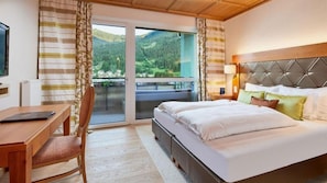 A hotel room with a bed, a desk, a chair, a TV, and a balcony with a mountain view.