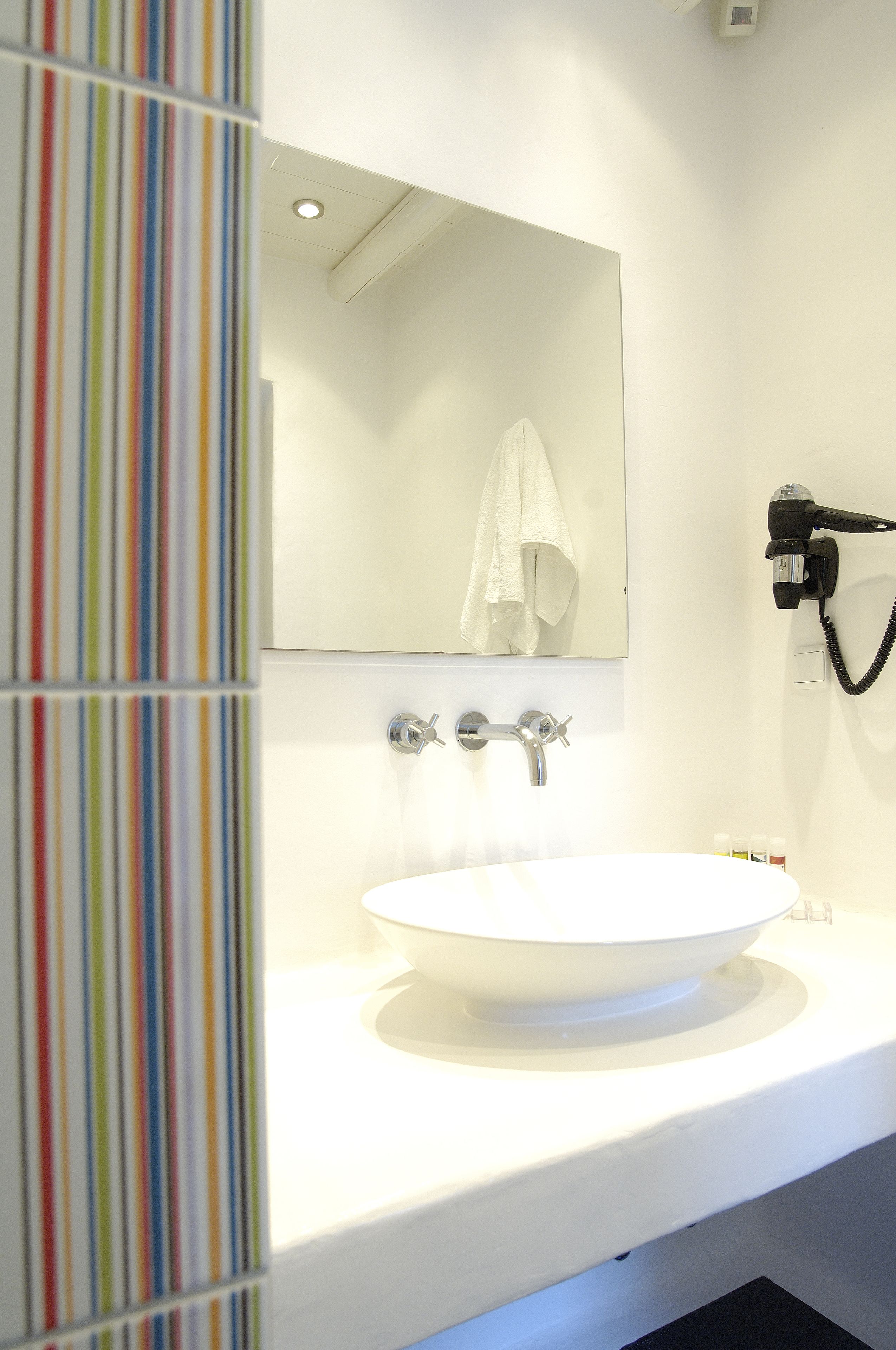 A bathroom with a white sink, a mirror, and a hairdryer mounted on the wall.