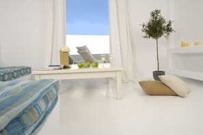 A modern living room with a white sofa, a white coffee table, and a small potted plant. - Kapetan Tasos Suites (Milos)