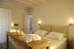 Habitación de hotel con un banco de madera, una mesita de noche con velas y una cama con ropa de cama blanca.