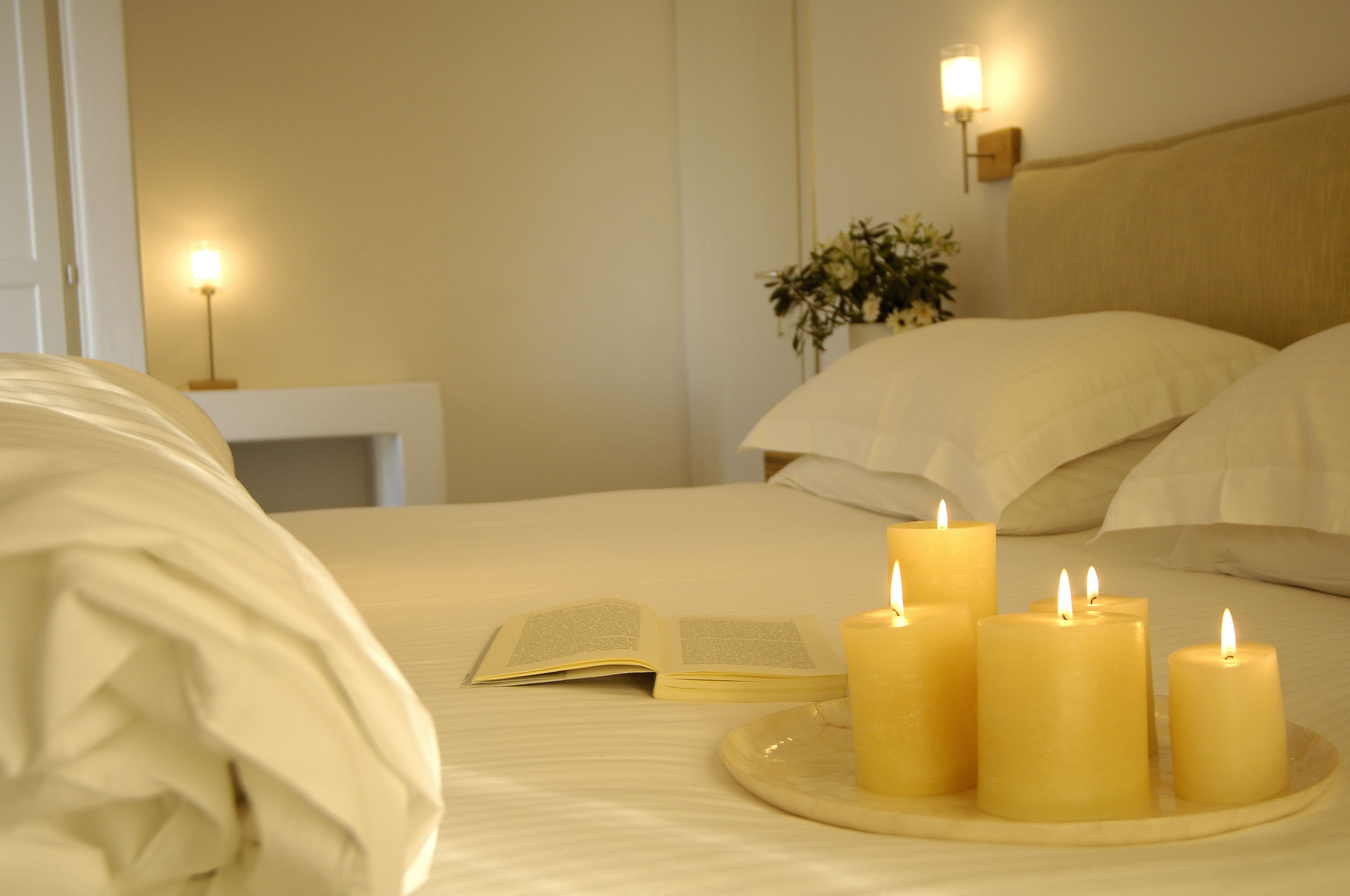 Una cama bien hecha con un libro abierto y cuatro velas encendidas sobre una bandeja.