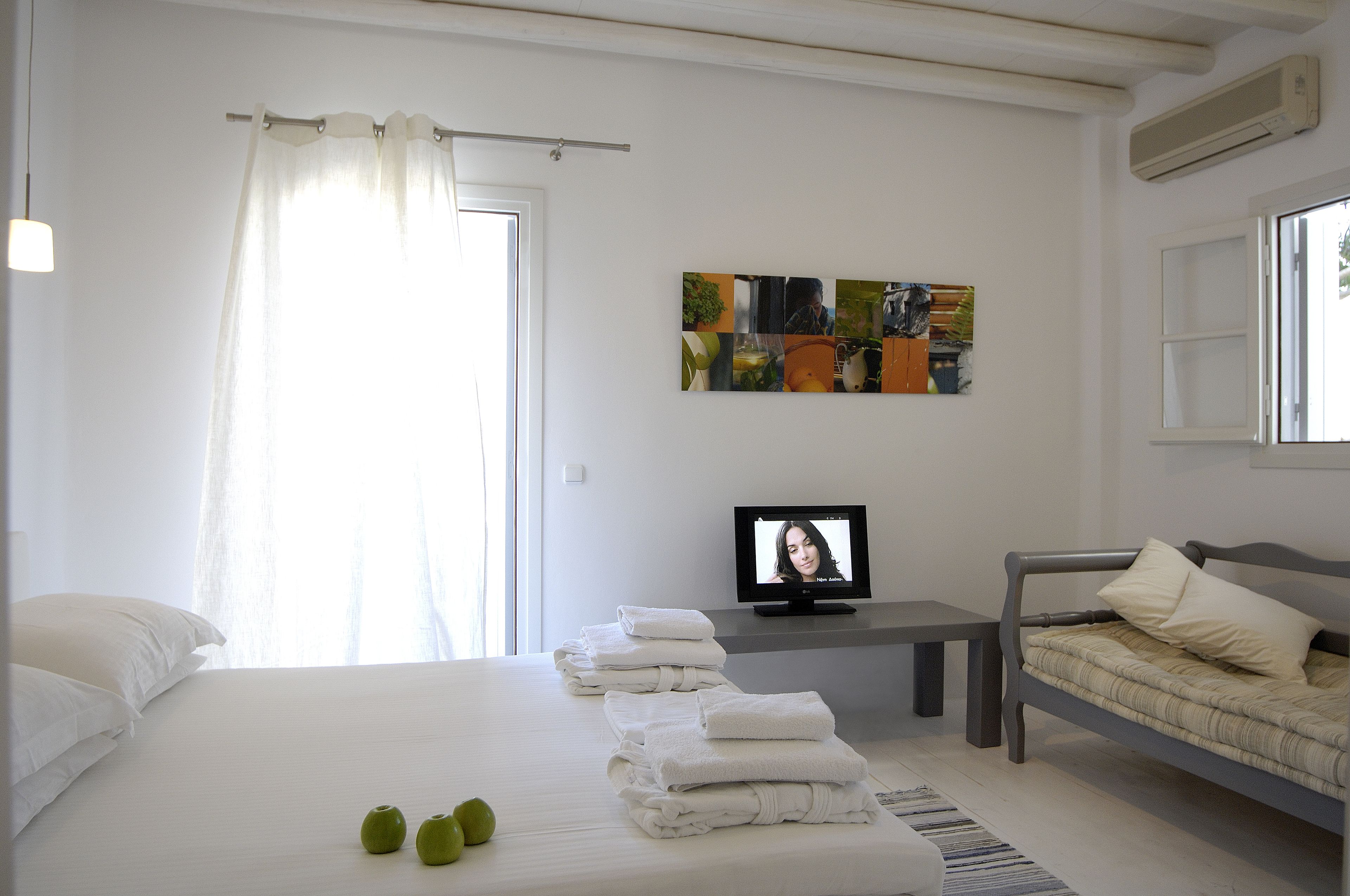 A hotel room with a bed, a TV, a desk, and a painting on the wall.