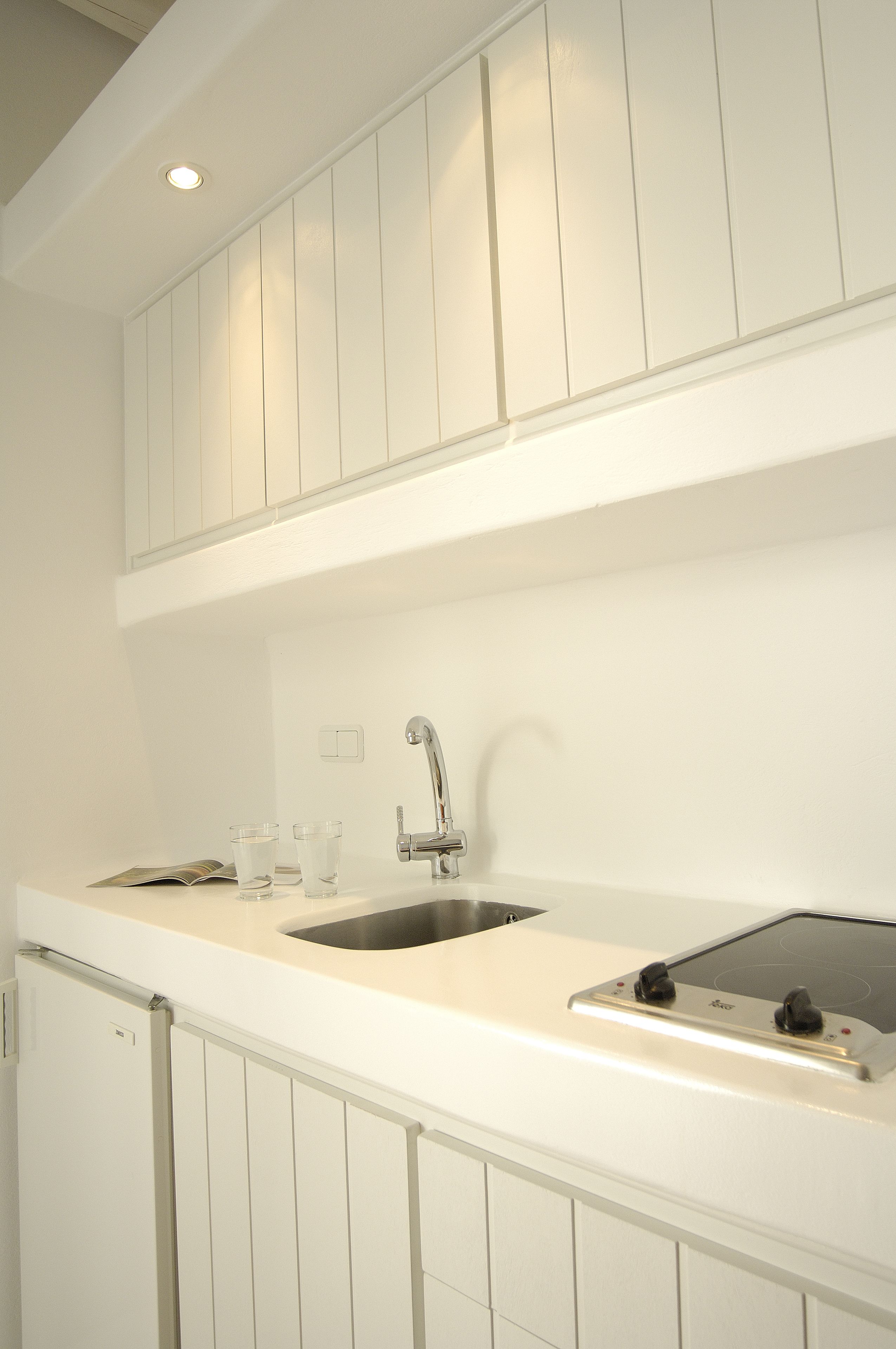 Cucina con mobili bianchi, lavello in acciaio inossidabile e piano cottura integrato.