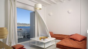 A modern room with a white table, orange cushions, and a view of the sea. - Kapetan Tasos Suites (Milos)