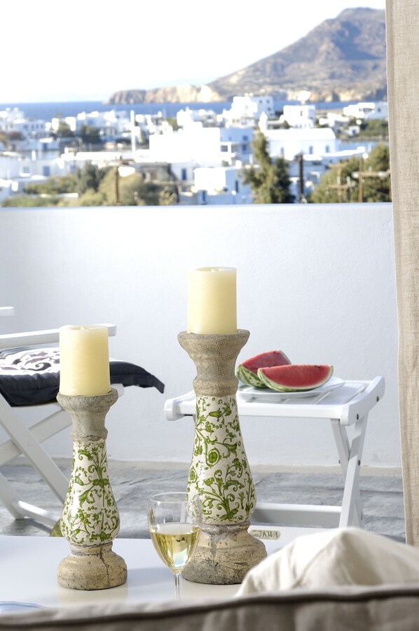 A balcony with two candles on decorative stands, a glass of white wine, and a plate with watermelon slices. - Kapetan Tasos Suites (Milos)