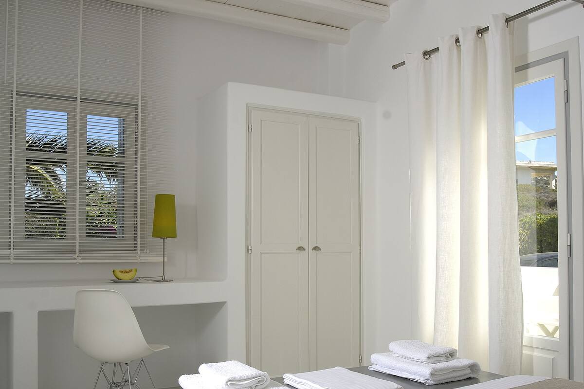 A modern hotel room with a bed, a desk, a chair, and a window with blinds.