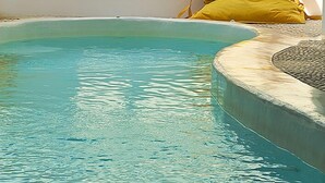A swimming pool with a clear blue water surface, a yellow bag, and a white wall with a shadow pattern. - Kapetan Tasos Suites (Milos)