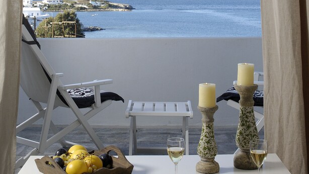 A balcony with a view of the sea, a table with a fruit basket, two candles, and a magazine. - Kapetan Tasos Suites (Milos)