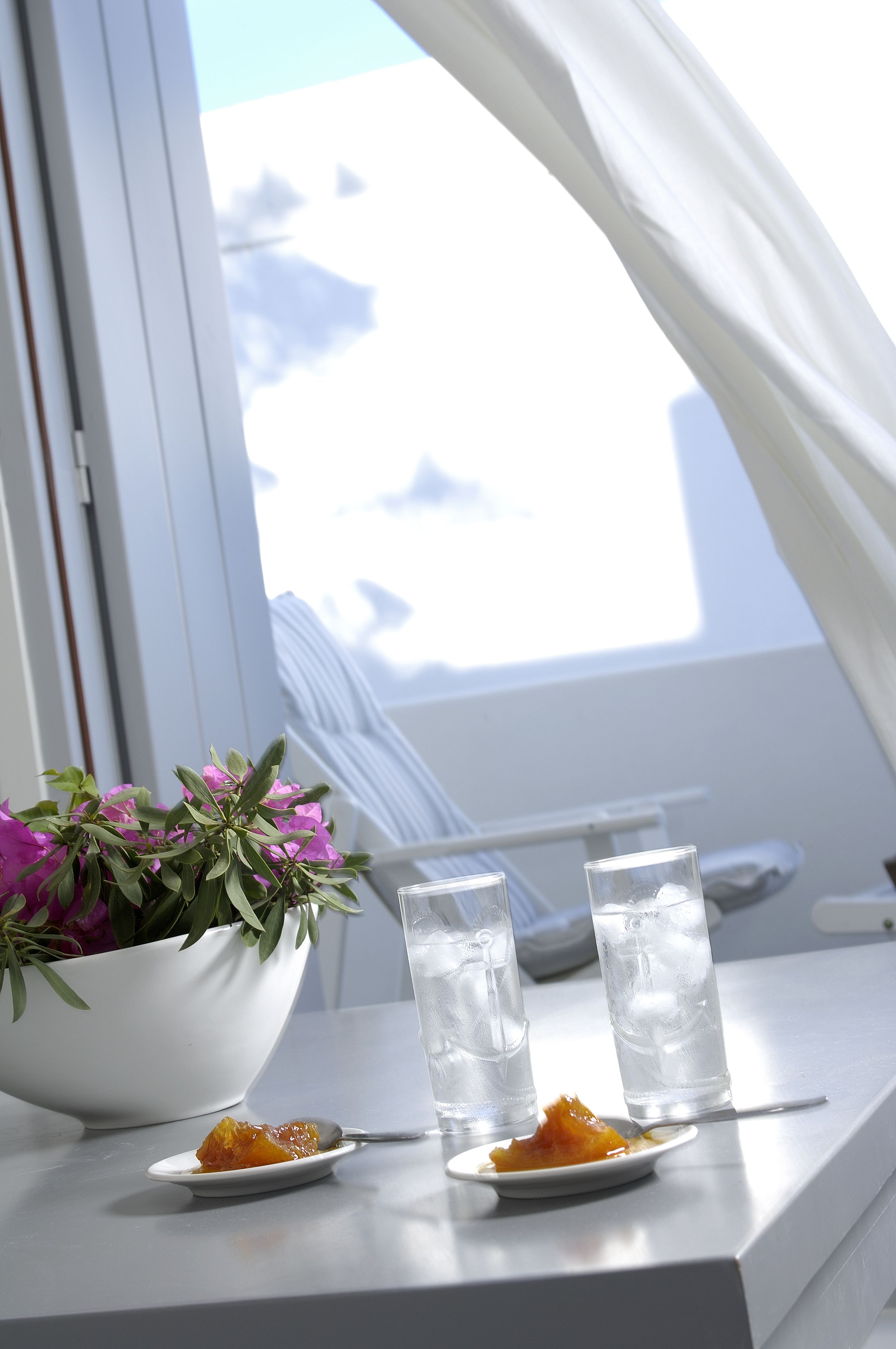 A table with two glasses of water, a bowl of flowers, and a plate with food.