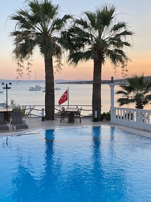 A poolside area with a view of the sea, palm trees, and a flag. - Cunda Panorama Hotel (Ayvalik)