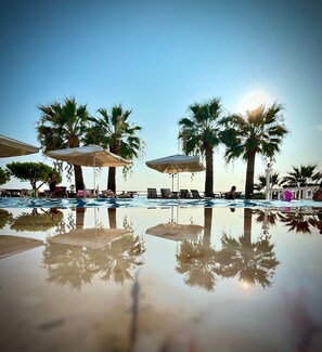 A pool area with palm trees and umbrellas, reflecting the surroundings. - Cunda Panorama Hotel (Ayvalik)