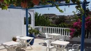Une terrasse extérieure avec des tables et des chaises blanches, une pergola bleue et des plantes en pot.