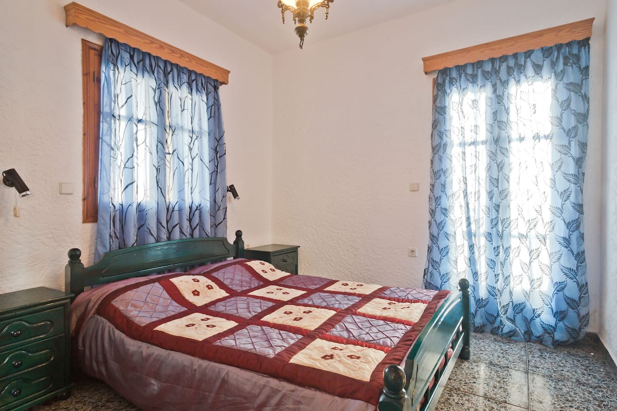 A bedroom with a bed, wooden headboard, green nightstand, and a window with blue curtains.