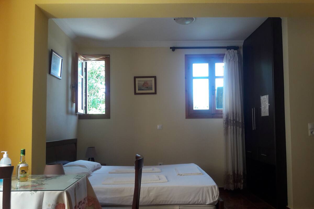 A hotel room with a bed, a chair, a table with toiletries, a window with curtains, and a door.