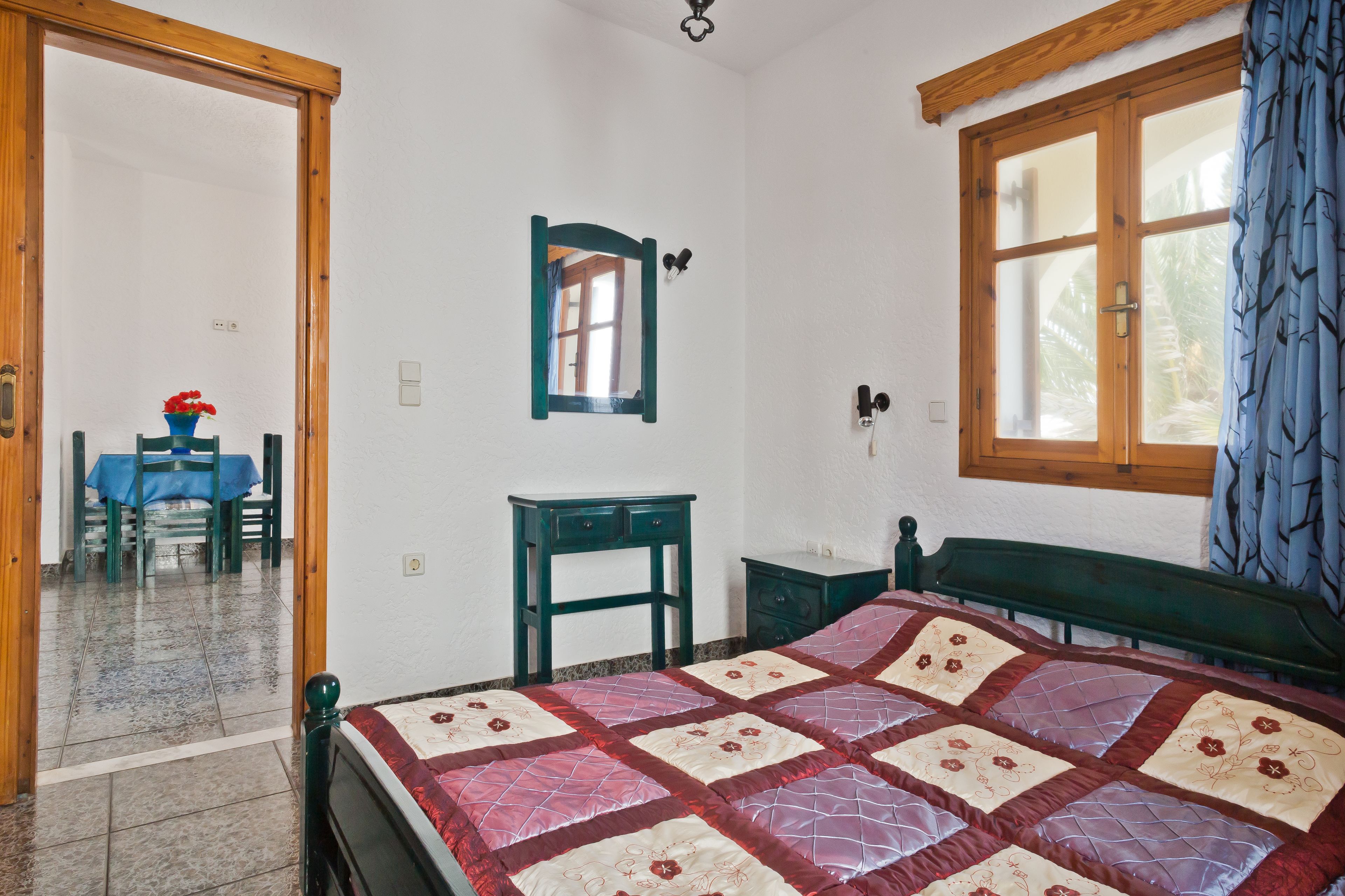 Un dormitorio con una cama, una ventana con cortinas, una mesita y una silla.