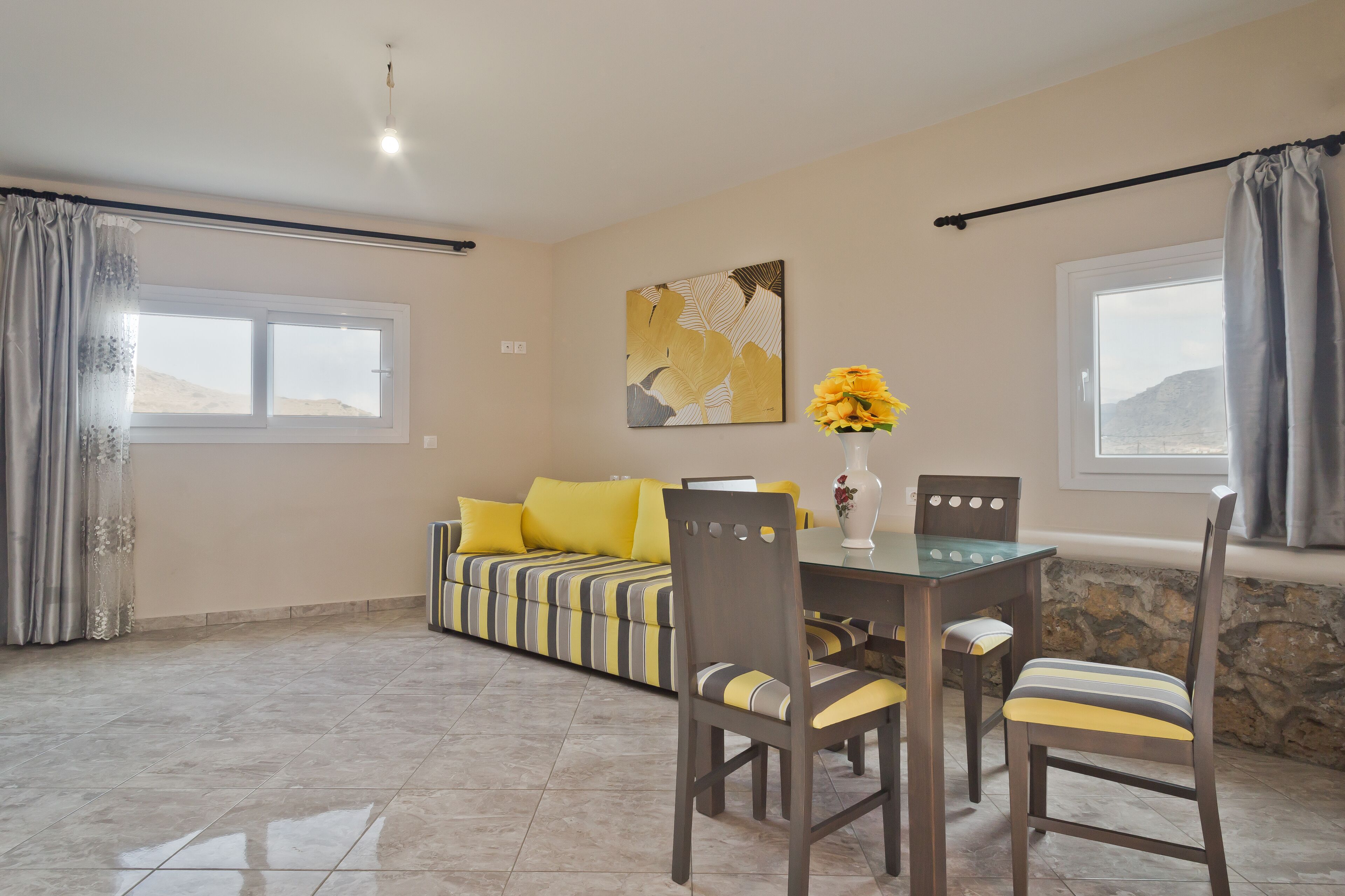 A dining area with a table, chairs, a sofa, and a vase with flowers.