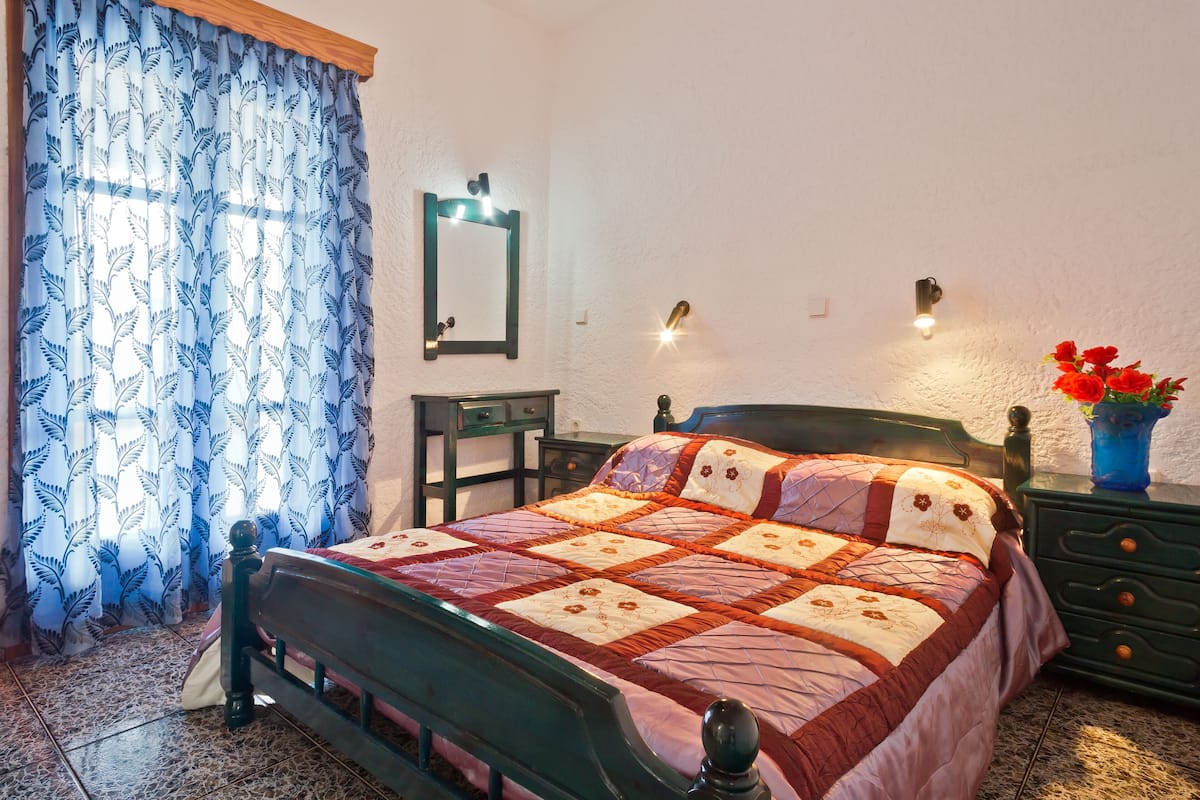 A bedroom with a bed, a nightstand, a dresser, a mirror, and a window with curtains.