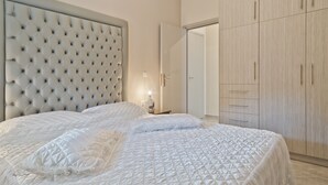 A bedroom with a tufted headboard, a large bed with white bedding, and a wardrobe with multiple doors. - Montemar Studios & Apartments (Karpathos)