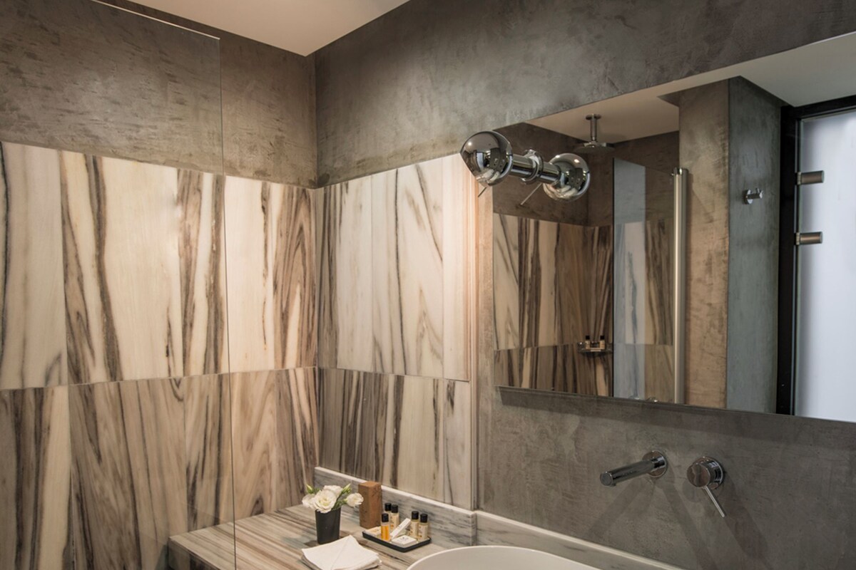 Un baño moderno con pared de mármol, un espejo grande y un lavabo blanco.