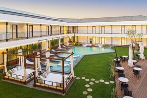 Un hotel con zona de piscina, mobiliario exterior y un jardín cubierto.